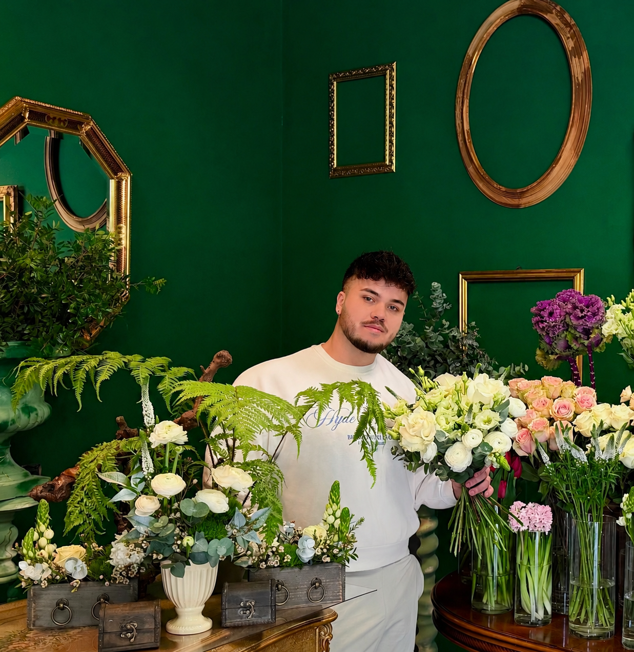 il proprietario nel negozio di fiori Mako Flowers, circondato da diverse composizioni floreali su un tavolo.
