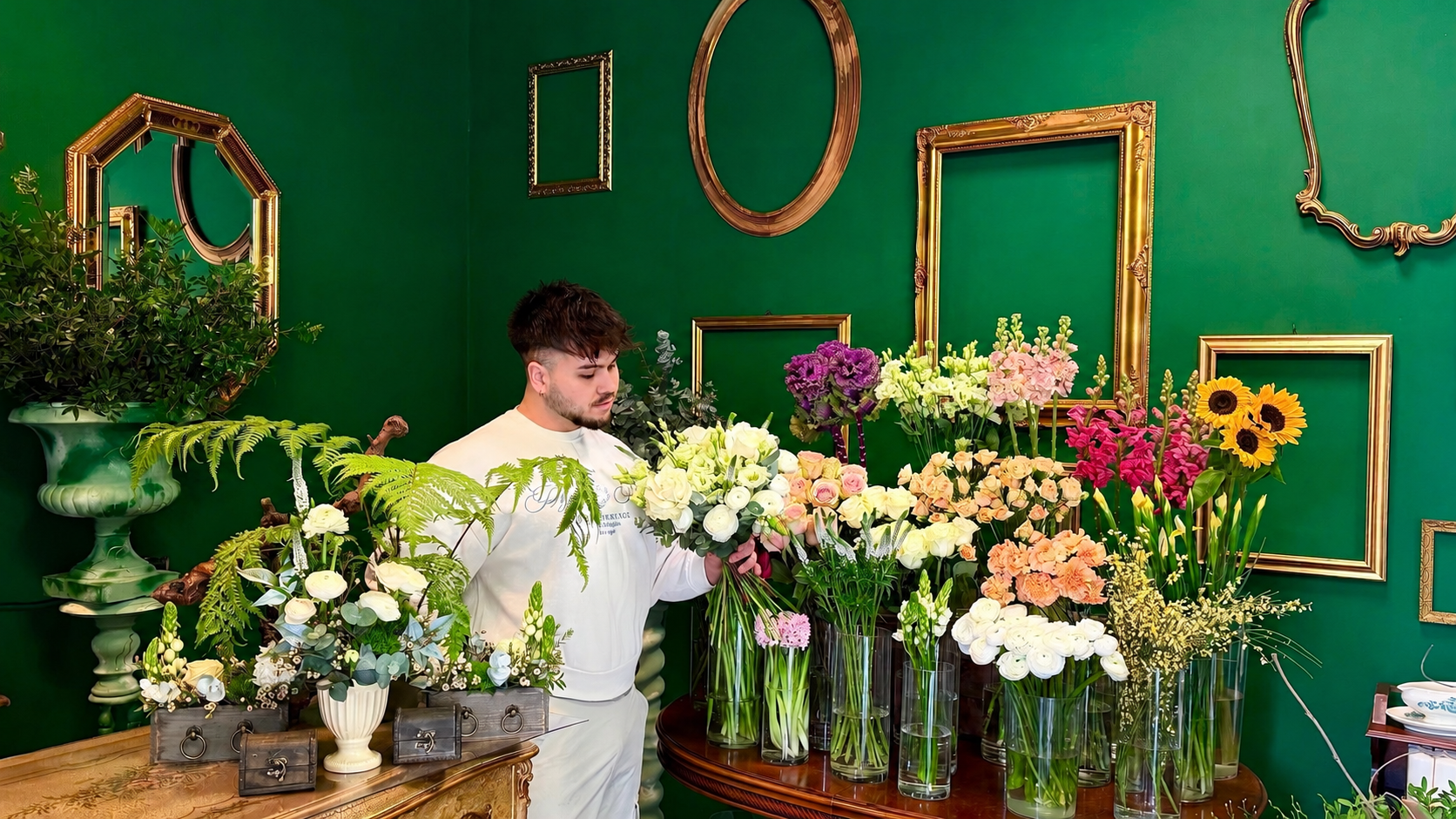 il proprietario nel negozio di fiori Mako Flowers, circondato da diverse composizioni floreali su un tavolo.
